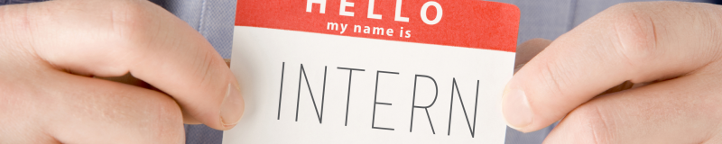 Close up of the front of a shirt pocket with two hands holding a sticker over the pocket. The sticker says "Hello, my name is intern"