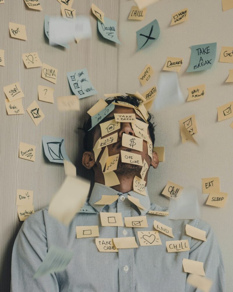A man leaning against a wall with sticky notes over his face and up the wall
