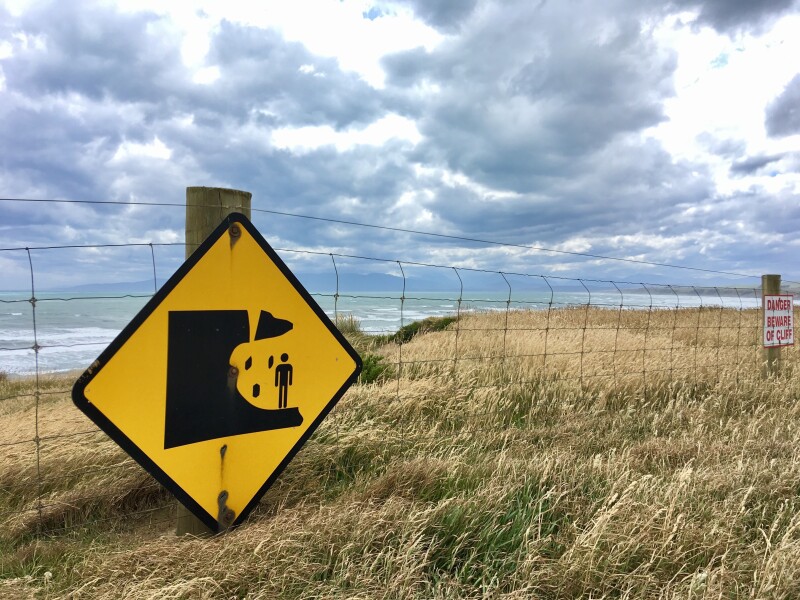  A yellow and black sign, warning of erosion, attached to a fence at the beach