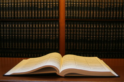 Book open on a desk with shelved books behind the desk