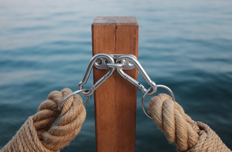 Two thick, heavy duty ropes (one going to the left and one to the right) are attached to a wooden post with carabiner clips. Water is in the background.