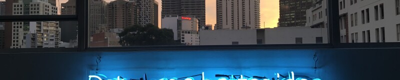 View of city skyline at twighlight through a window. Below the window is a blue neon sign saying "data has a better idea". The last "a" in data is not lit up.