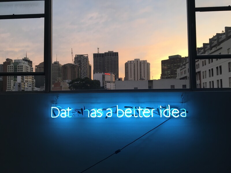 View of city skyline at twighlight through a window. Below the window is a blue neon sign saying "data has a better idea". The last "a" in data is not lit up.