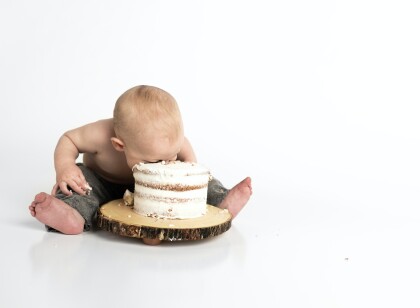 Baby sitting on the floor with its face in a cake