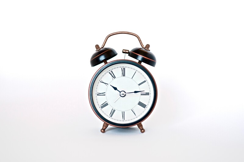 Old-style wind-up alarm clock with roman numerals reading 10:14, on a white background