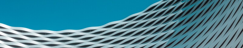 Looking up at curved building with waves in the structure, a blue sky in the background