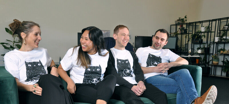 Four people sitting laughing on a couch wearing MadeCurious tee shirts