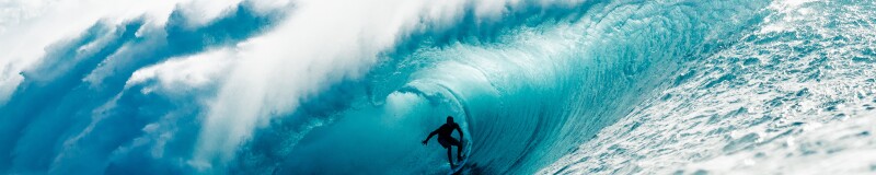 Side-long view of a large cresting wave with a surfer in the middle of the barrel