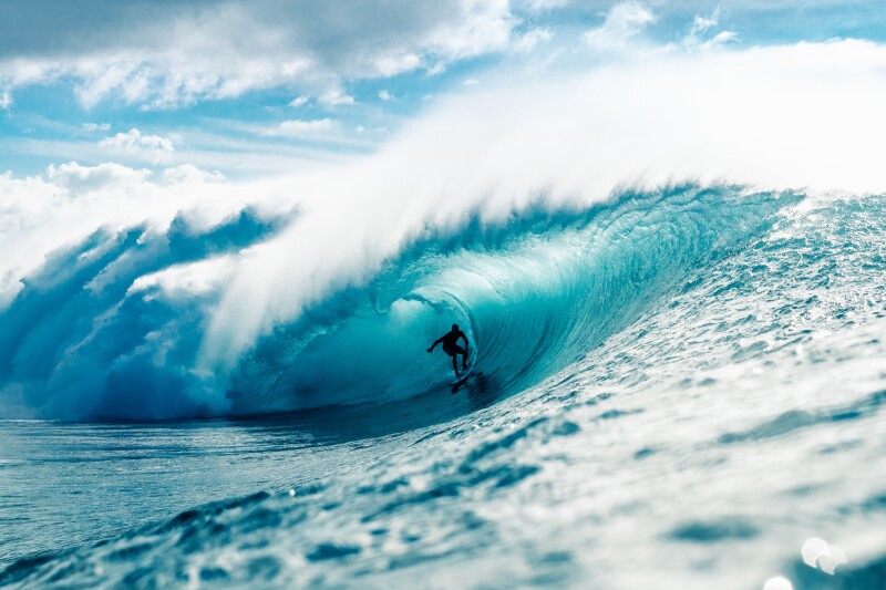 Side-long view of a large cresting wave with a surfer in the middle of the barrel