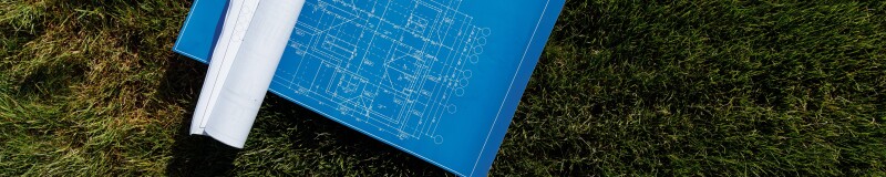 Unfurled blueprint on grass, rolled up plans lying on the left hand side of the blueprint