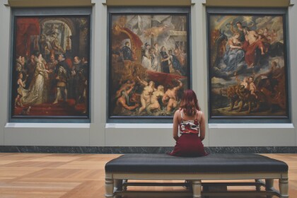 Woman sitting. on ottoman in front of three paintings