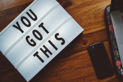 Light box on a table, to the left of a phone and and open laptop. Lightbox says "You got this"