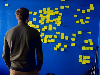 Person looking a a blue wall filled with yellow post it notes