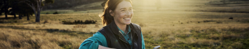 Woman leaning on a fence post in the country holding a device in one hand