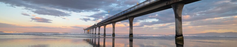 View of New Brighton pier from the beach, the tide is out and a pastel sunset is reflected on the sand