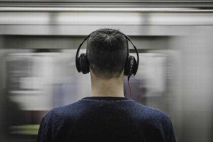 Person with headphones, blurred train passes