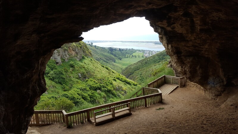 Looking out the mouth of a cave, green hills in the foreground, sea in the distance