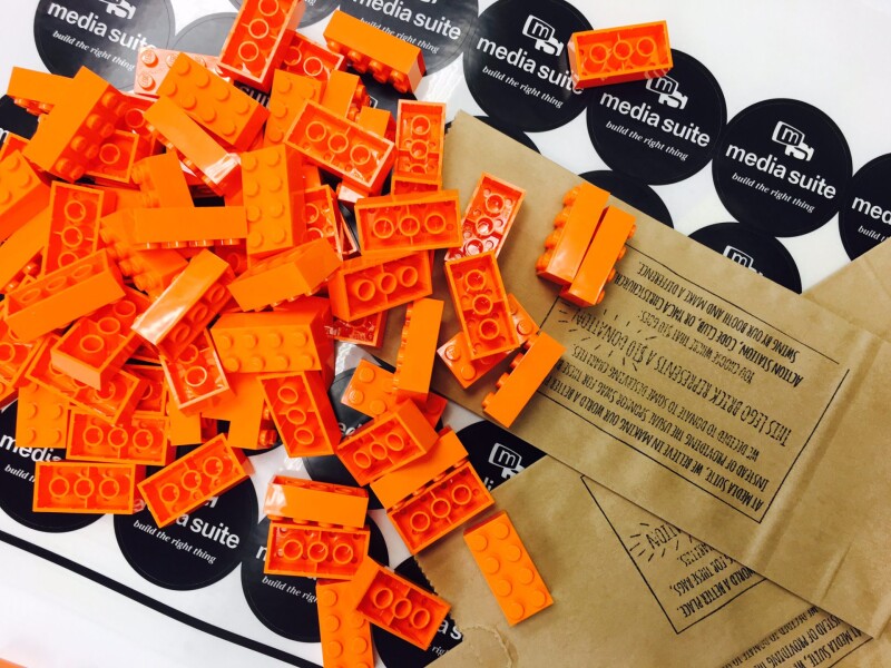 Orange lego, stamped brown envelopes on top of a sheet of Media Suite stickers