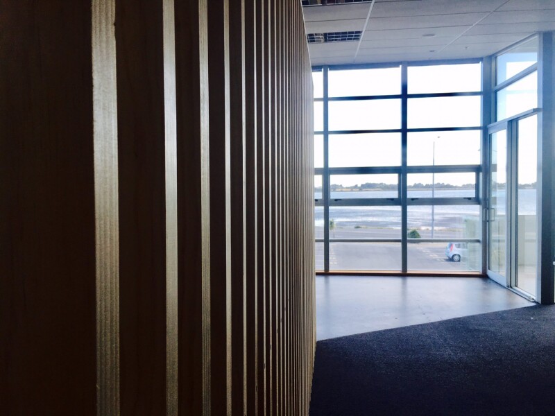 A view of an office corridor, with windows at the end of it, and timber screening to the left.