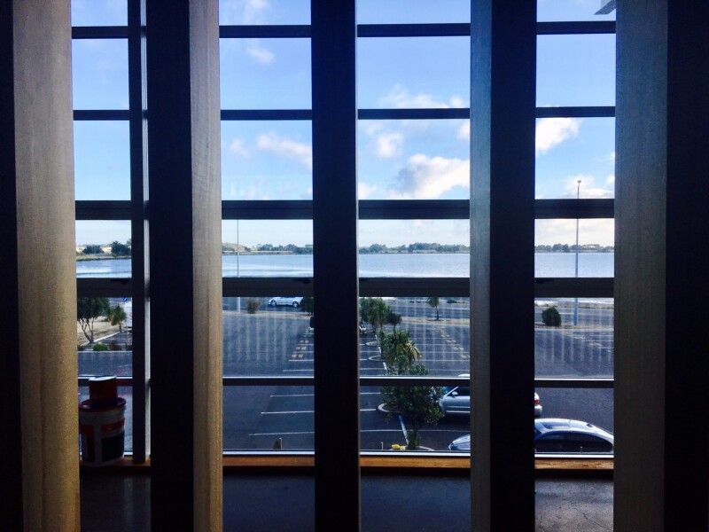 View through wooden screening and windows over a carpark to the water 