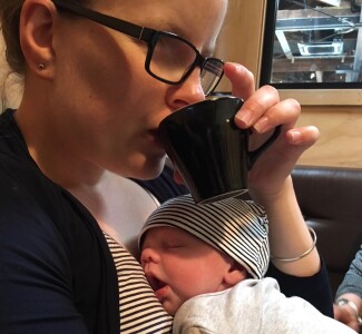 Abbie sipping a coffee with her baby sleeping on her chest