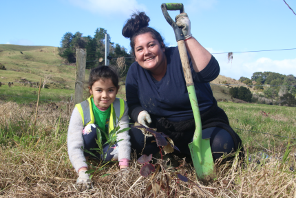 Mother and child kneeling in paddock holding a spade