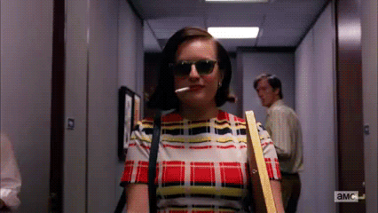 Gif of Peggy Olsen from TV show Mad Men strutting down the office hallway, sunglasses on and lit cigarette in her mouth.