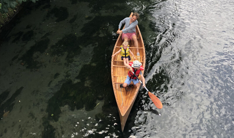Image taken from above of Dad in a wooden canoe on the water, with two small children