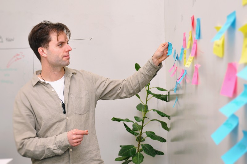 Person organising post it notes on white wall