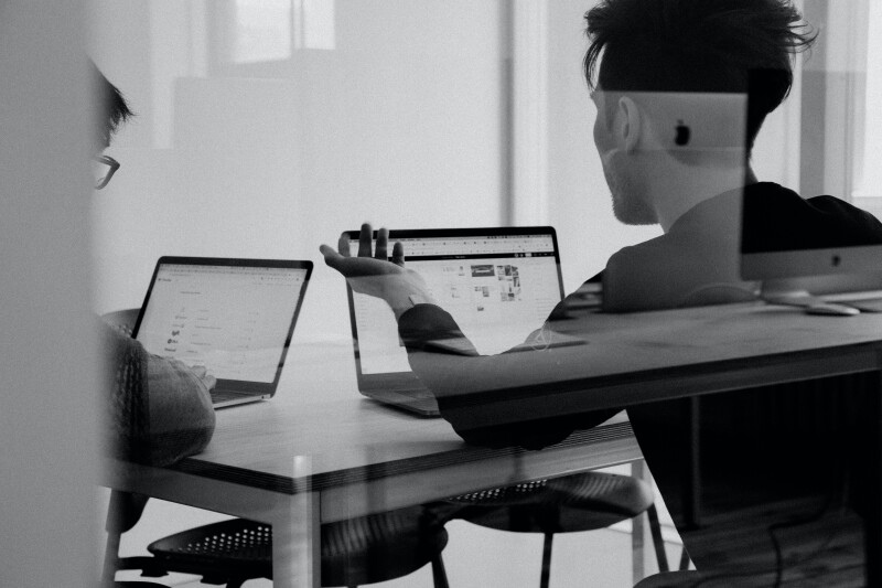 Black and white photo of two people discussing something while looking at a laptop